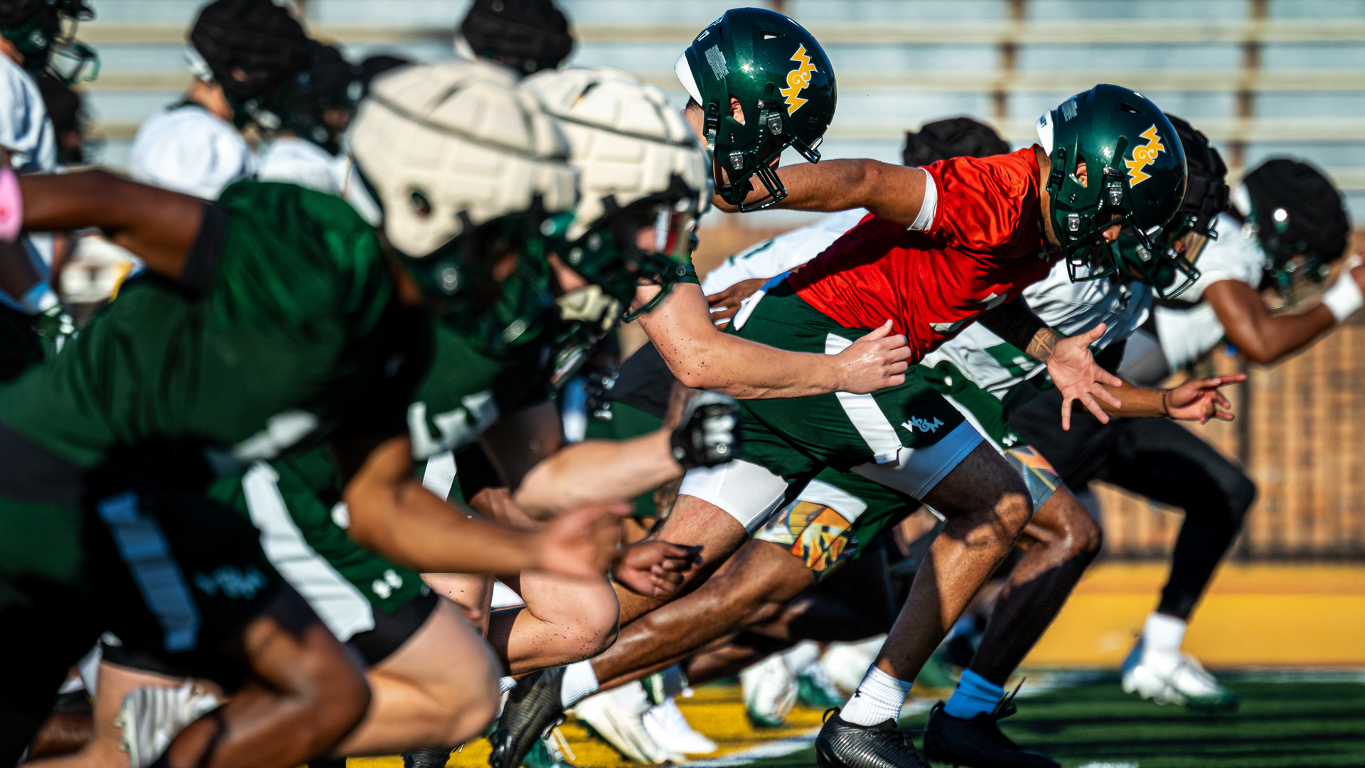 A group of W&M football players sprint in a line during practice at Zable Stadium