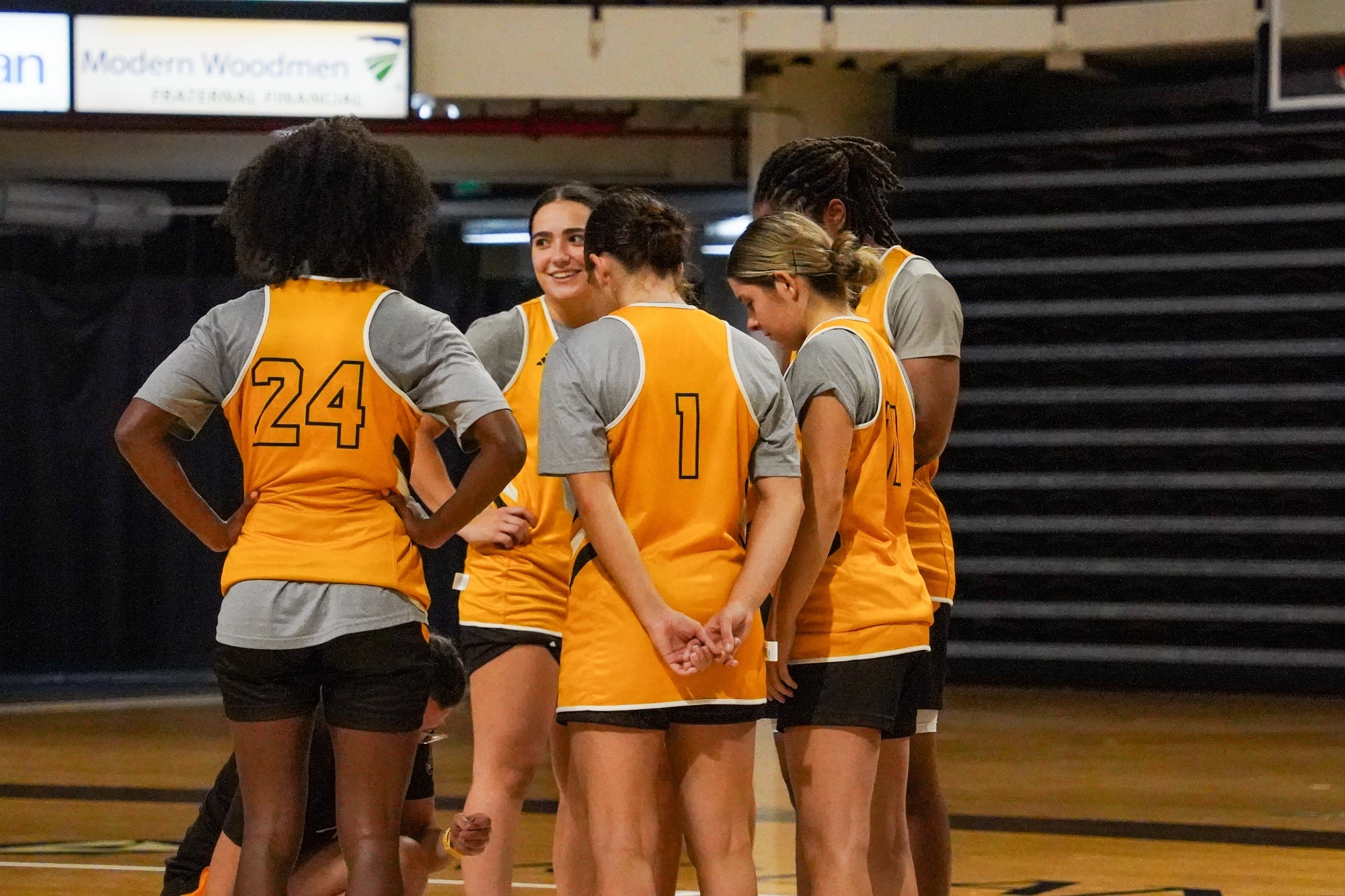Women's basketball players huddle around Head Coach Kate Achter during practice as she draws up a play