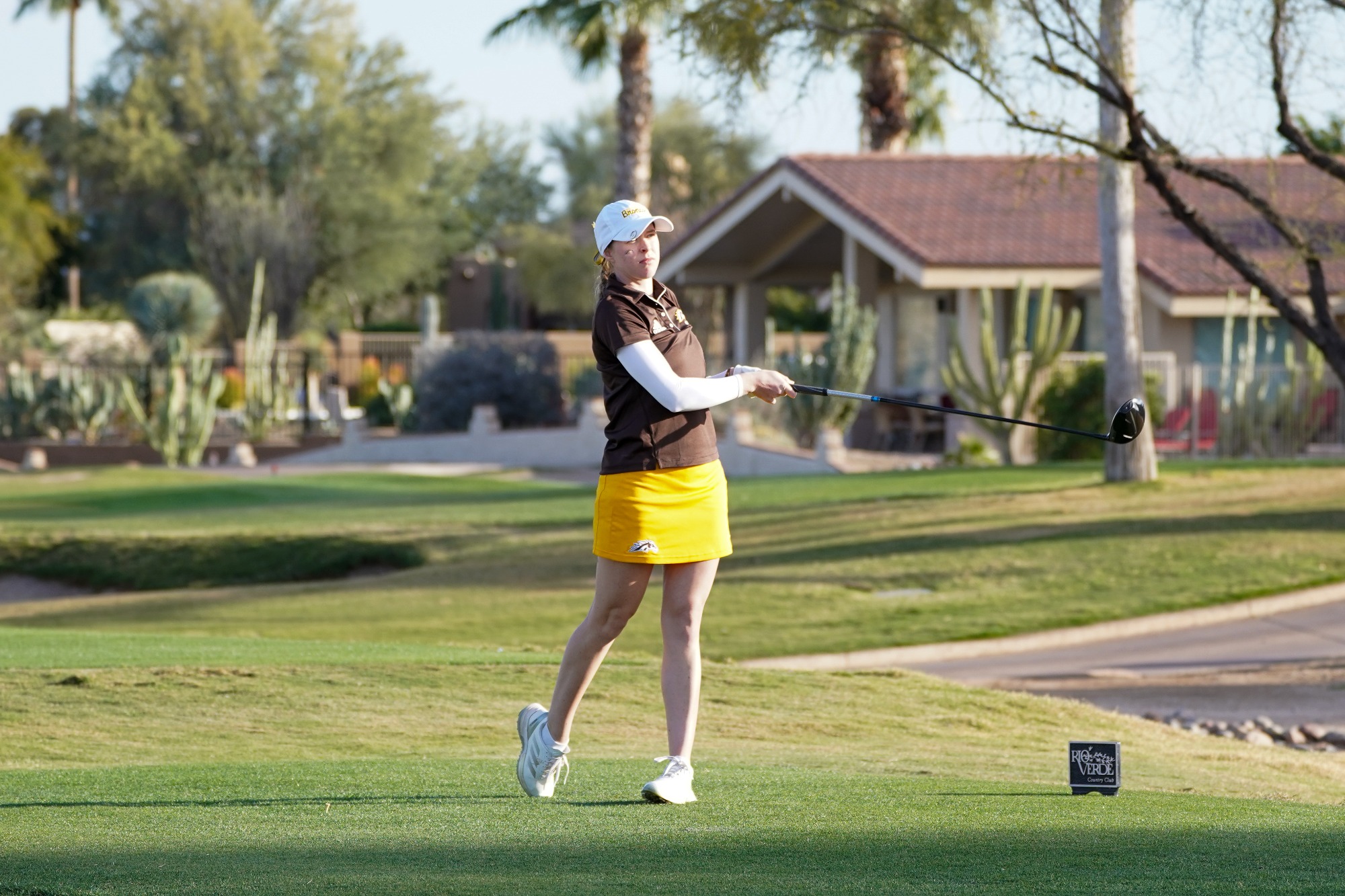 Jenna Hayes stands looking forward with her back leg on its toes after taking a driving swing at a golf ball