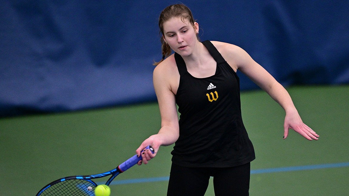 Sasha Riley swings her racquet, connecting on a tennis ball indoors