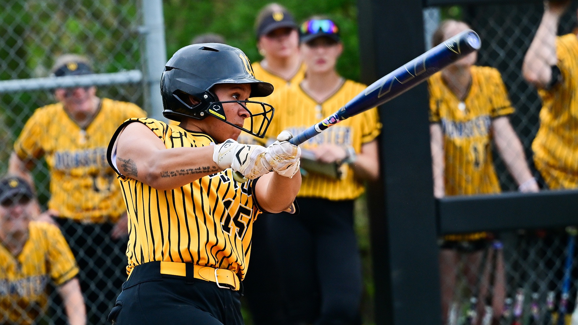 Jasmine Mueller swings through a pitch as the Wooster dugout looks on in the background