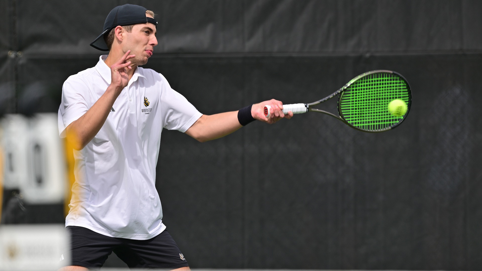 Andrew Wissman hits a forehand over a tennis net in the foreground