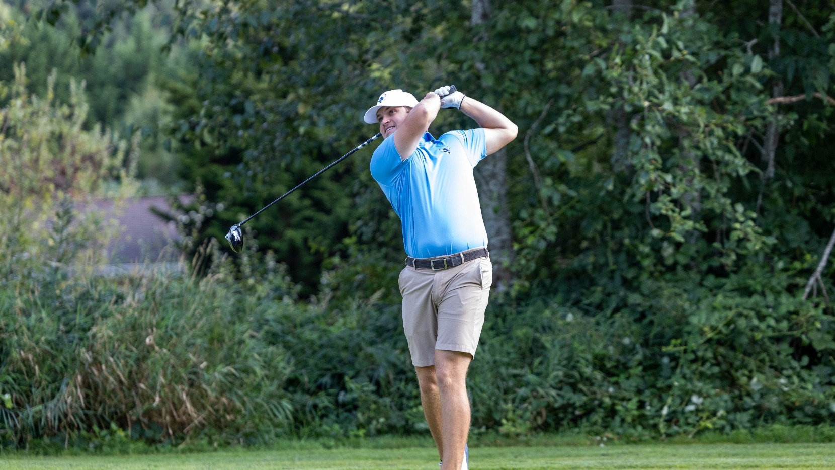 WWU men's golfer in light blue shirt swinging a driver on a golf course