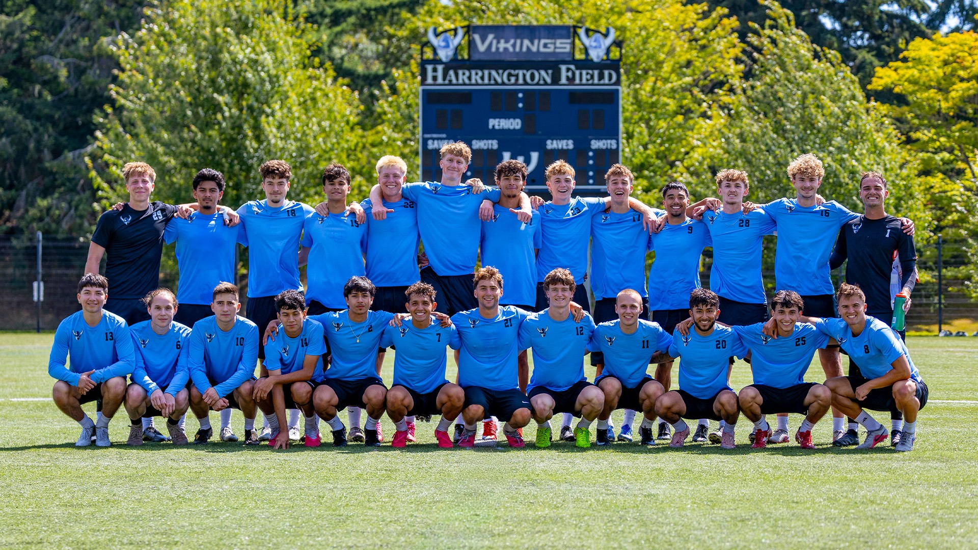 A soccer team poses for a photo on a field in front of a scoreboard.