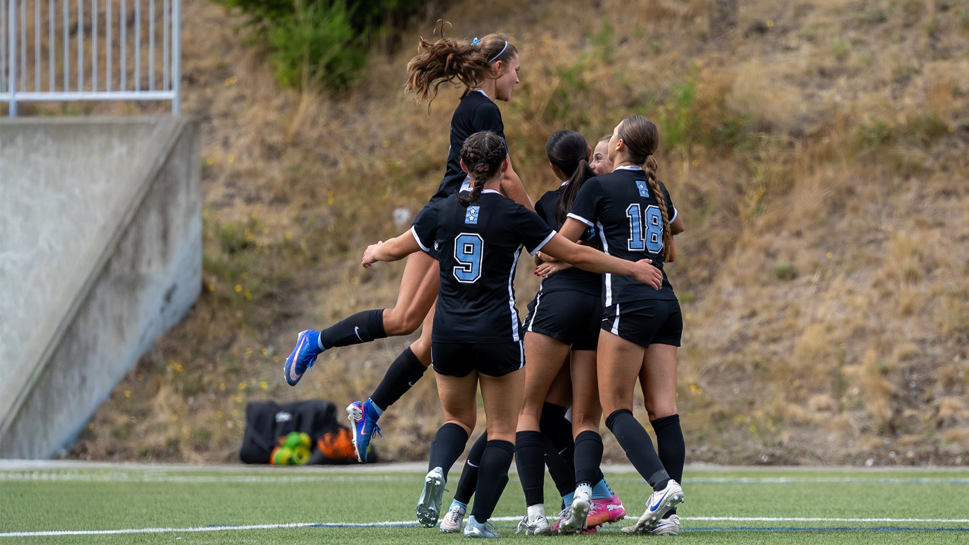 WWU team members celebrating and hugging each other on a turf field in a college soccer match