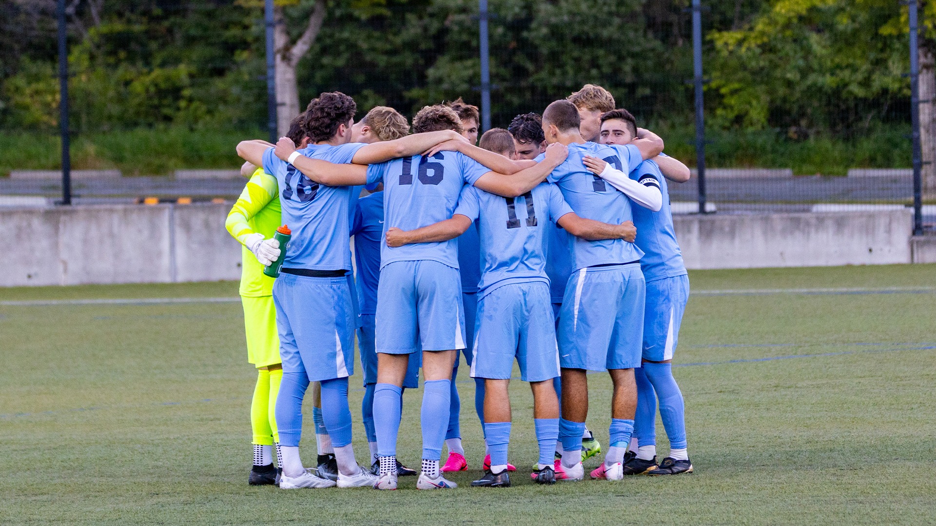 WWU men's soccer team in a huddle wearing light blue jerseys
