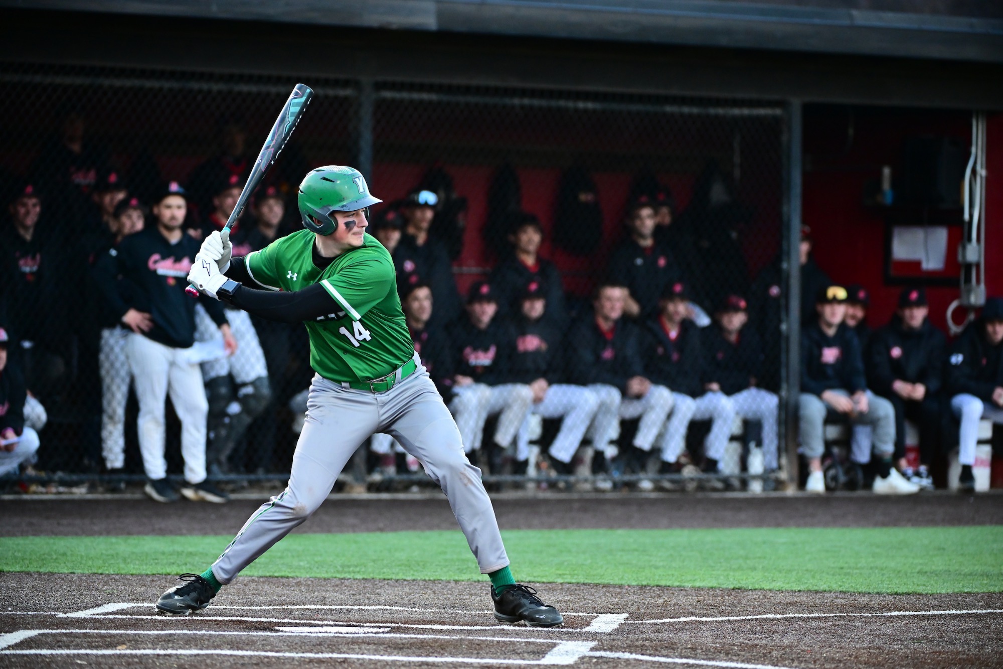 male in green uniform swinging baseball bat