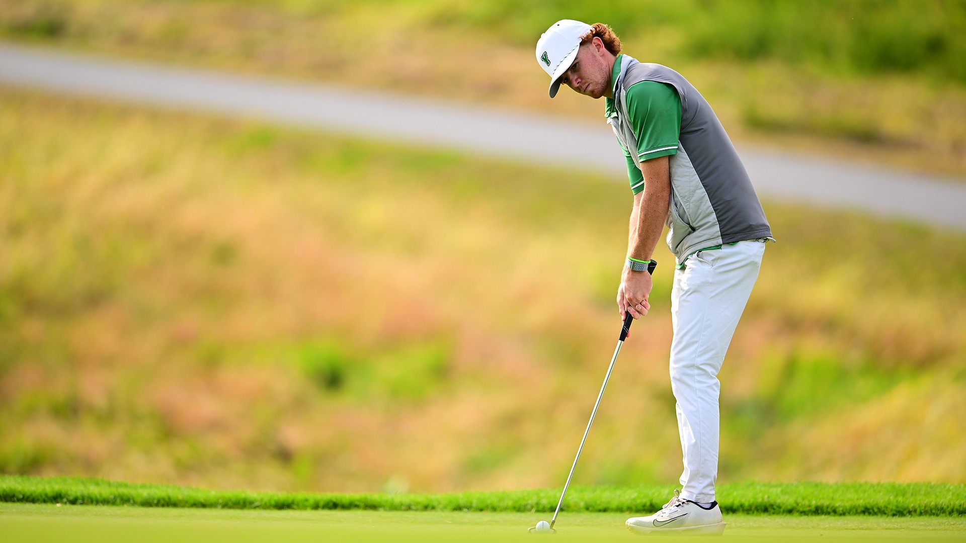 male golfer in grey vest puts ball