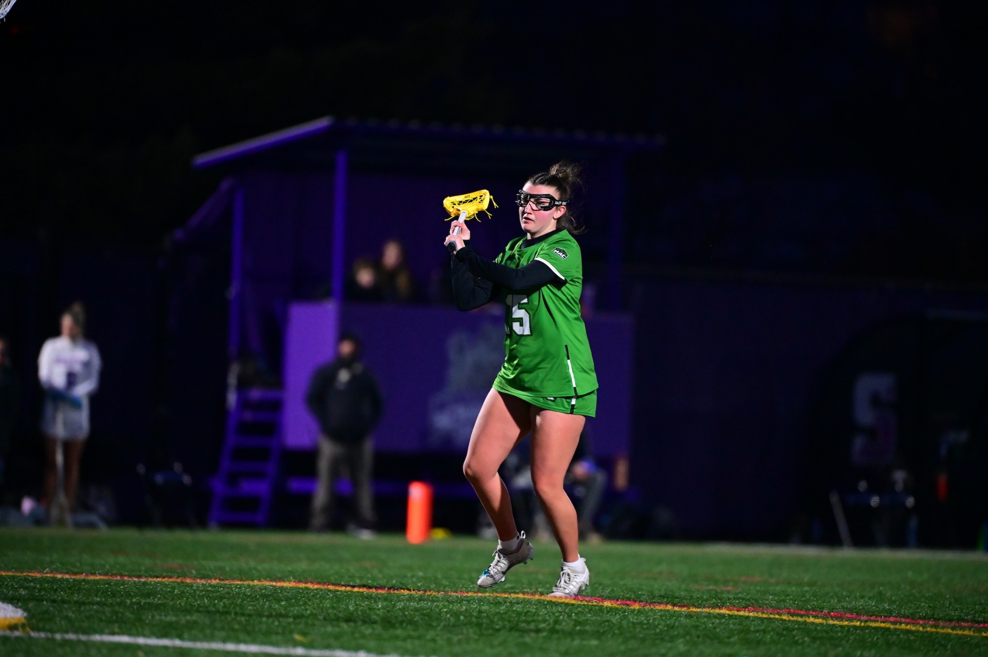 female in green uniform holding lacrosse stick