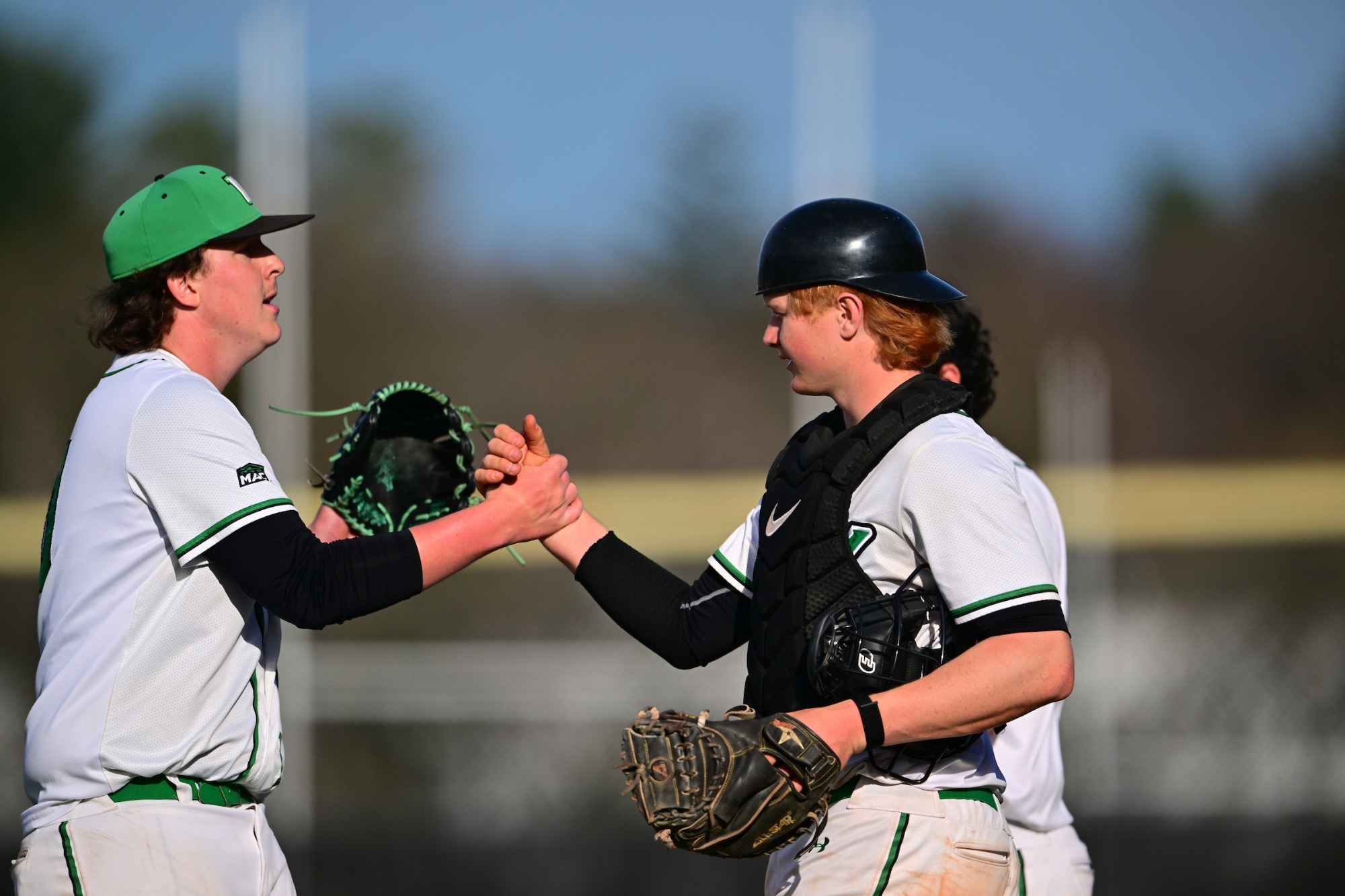 two males in white uniforms giving each other a high-five
