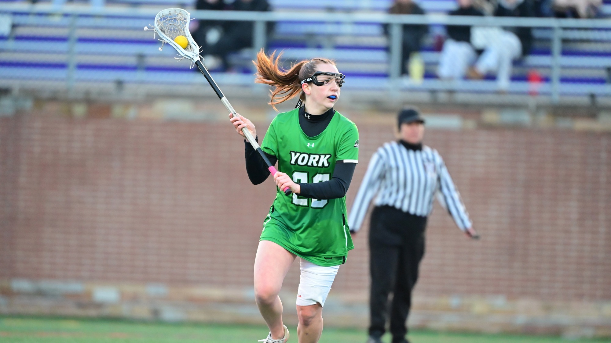 female lacrosse player in green uniform looks to make a pass