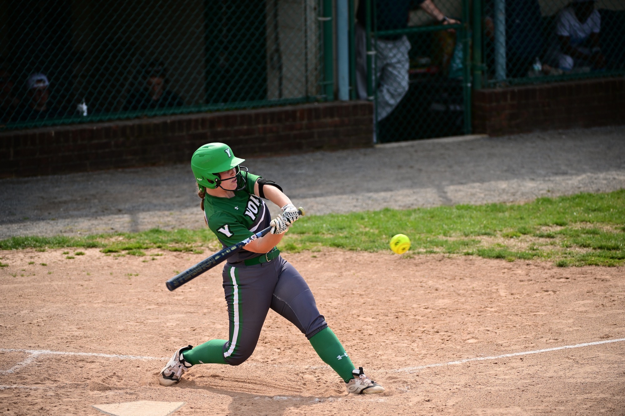 girl in grey and green uniform swinging softball bat