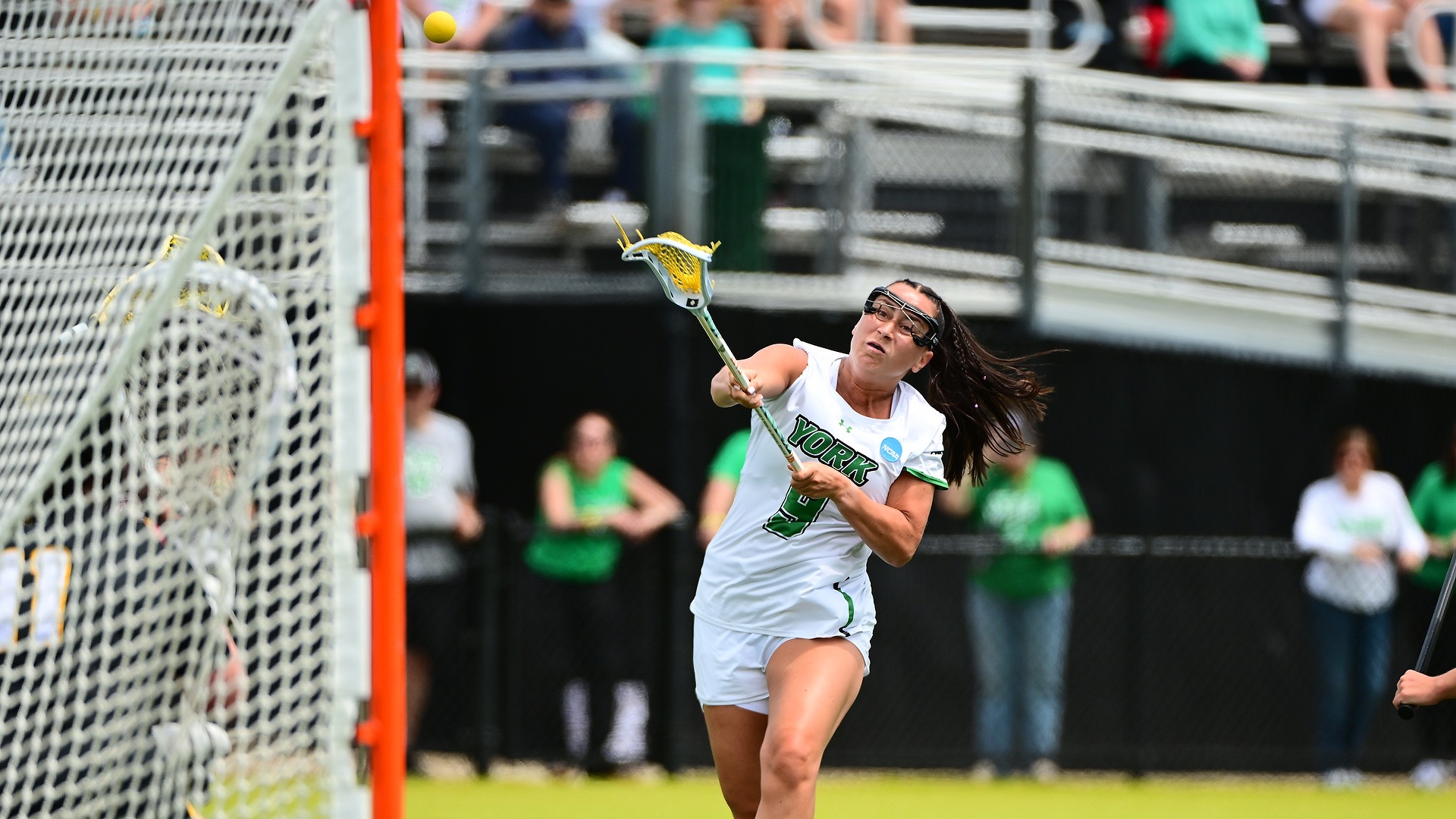 female lacrosse player propels shot towards goal