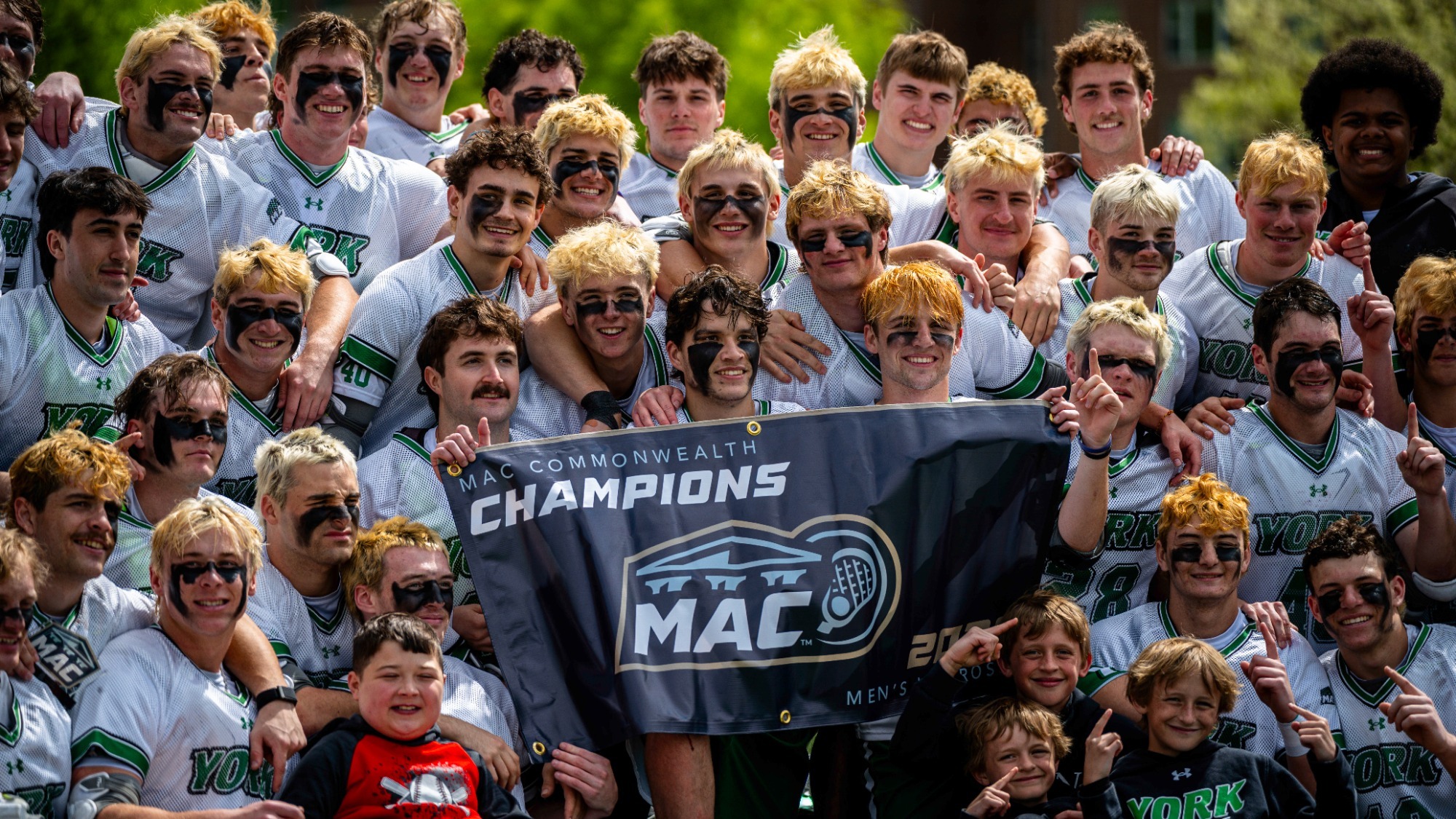 the men's lacrosse team poses for photo with championship banner
