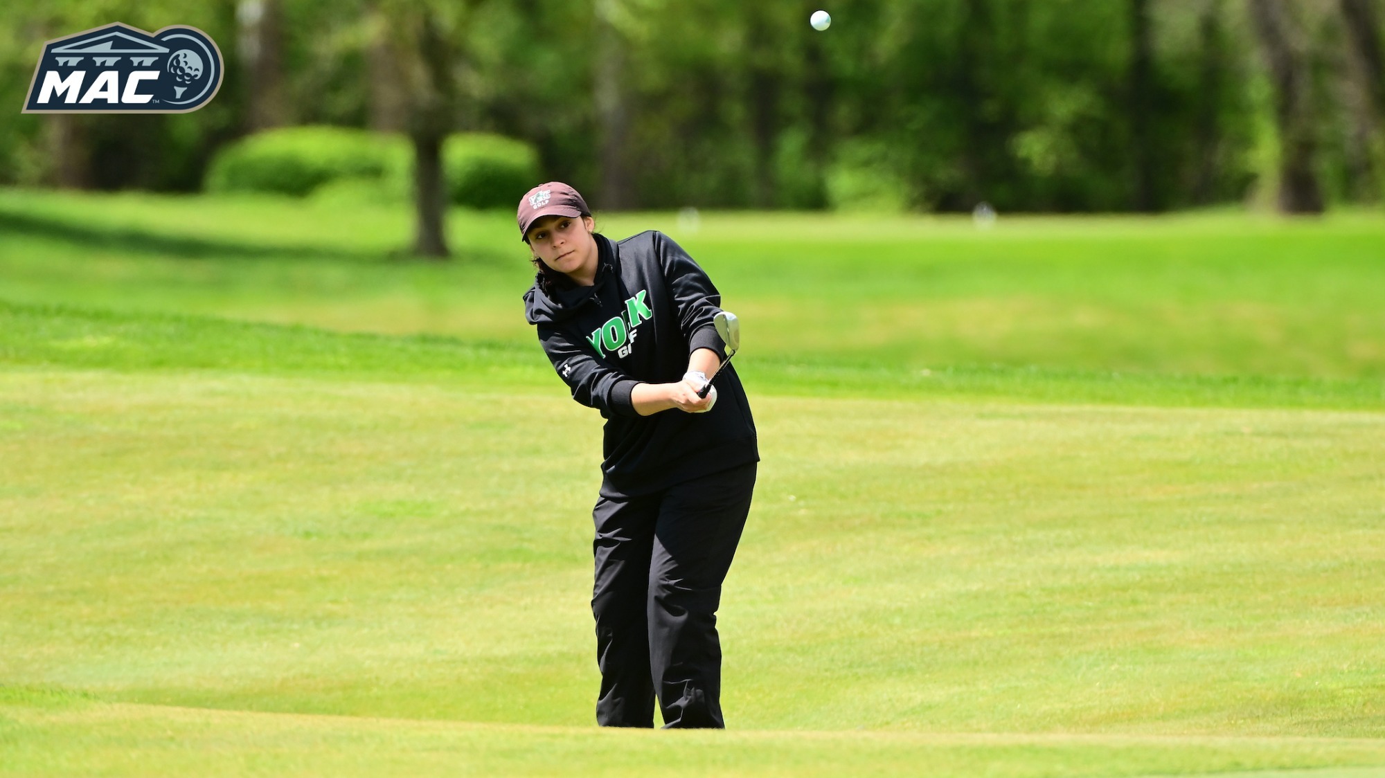 female golfer chips shot on to green with MAC logo in upper left corner