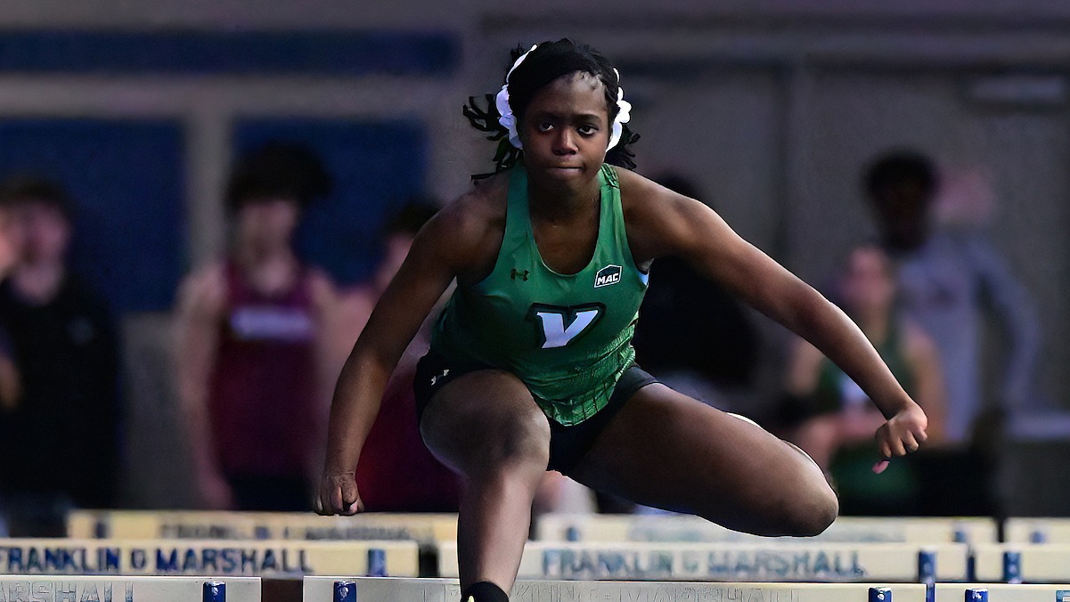female track and field athlete leaps over hurdle