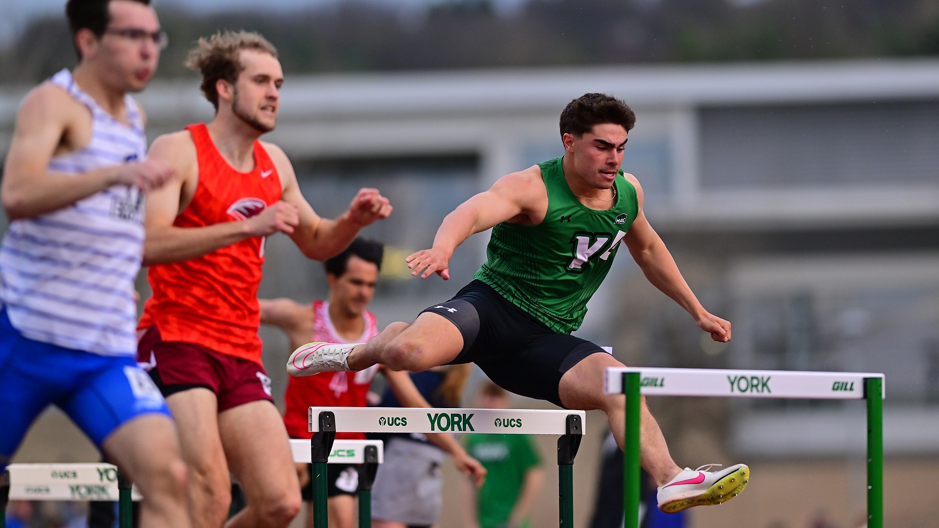 male track athlete leaps over hurdle at Graham Field