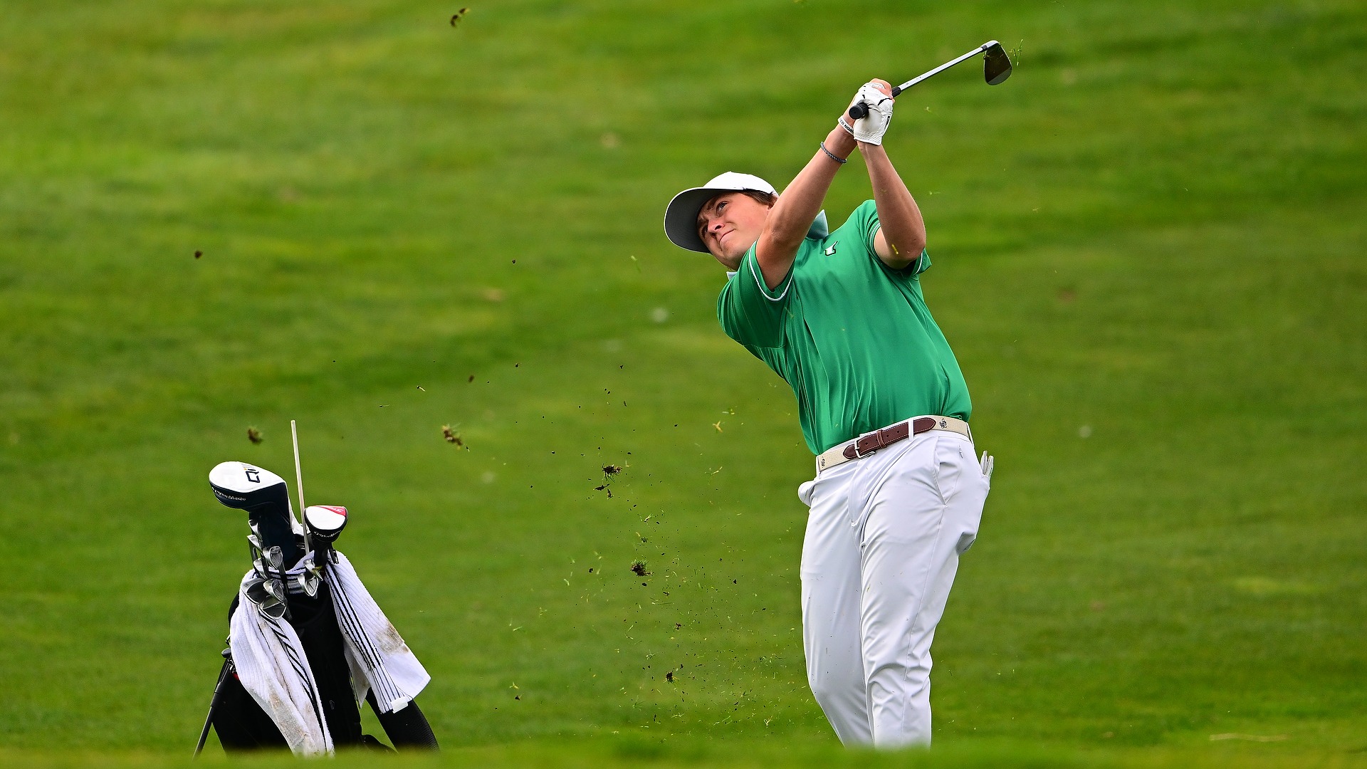 male golfer in green shirt tracks a wedge shot