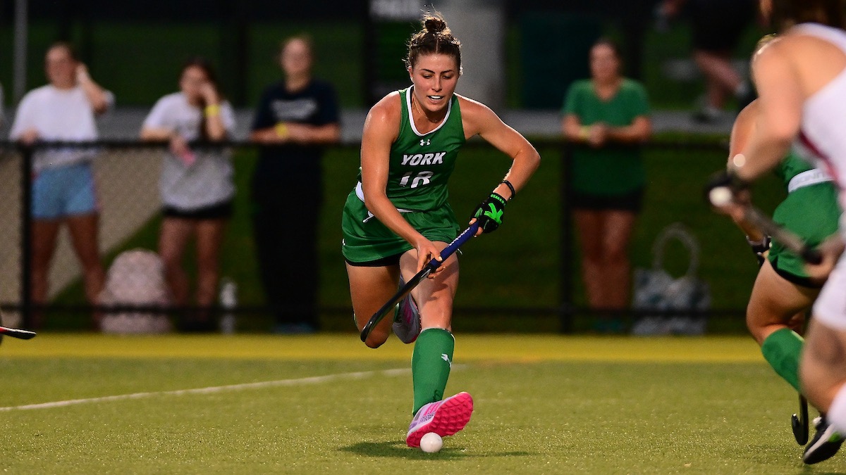 Female holding field hockey stick running with ball