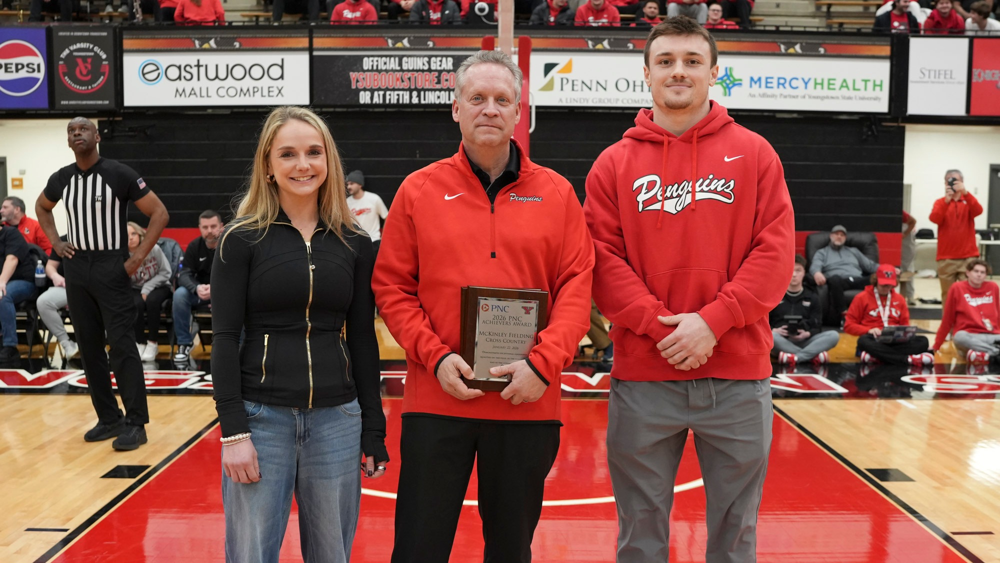 YSU cross country runner McKinley Fielding, Regional President for PNC Bank Ted Schmidt, and YSU football player Beau Brungard standing on a basketball court for the PNC Achievers Award.