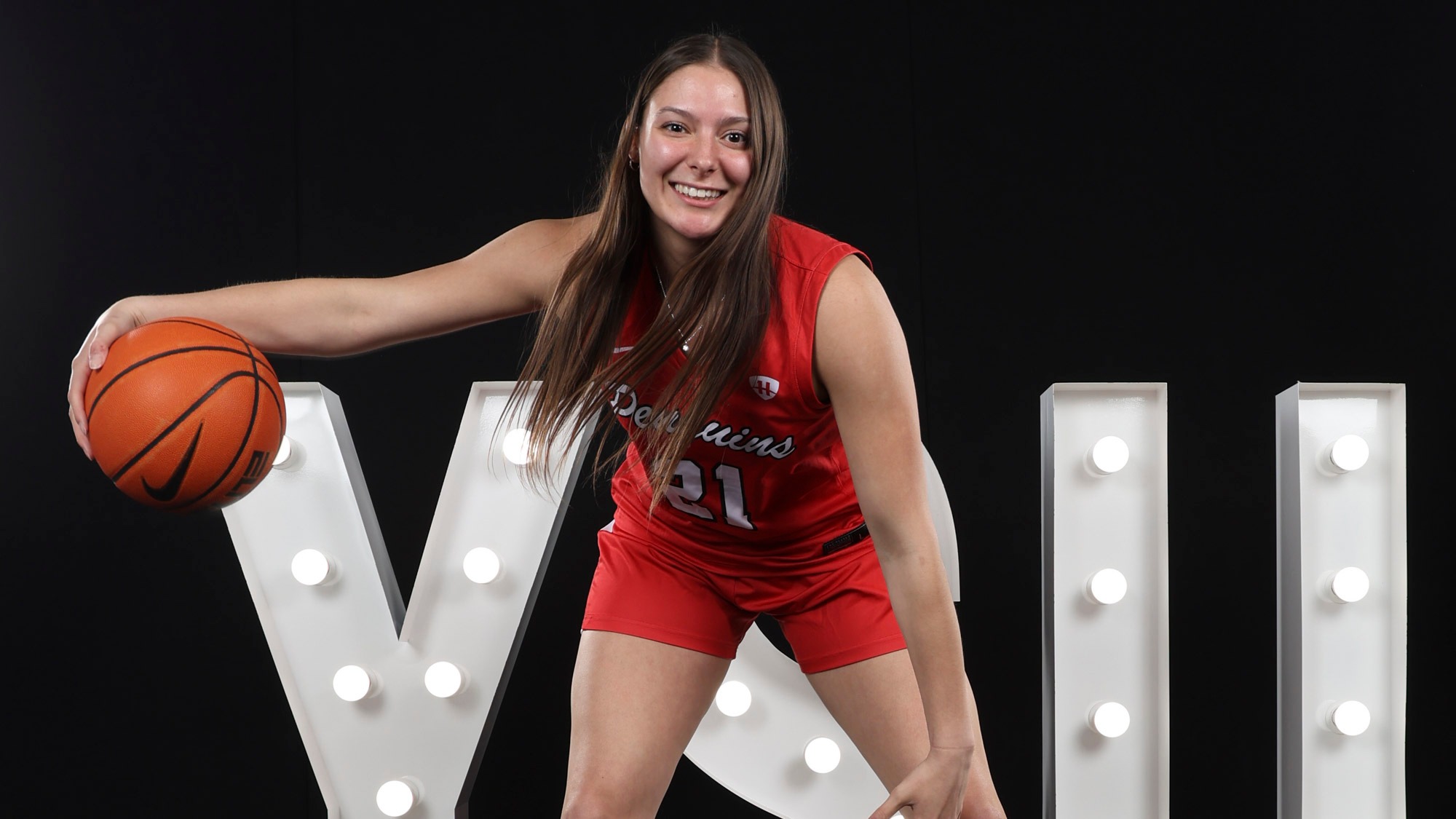 Mia Kalich dribbles a basketball in front of lit YSU letters in a studio setting.