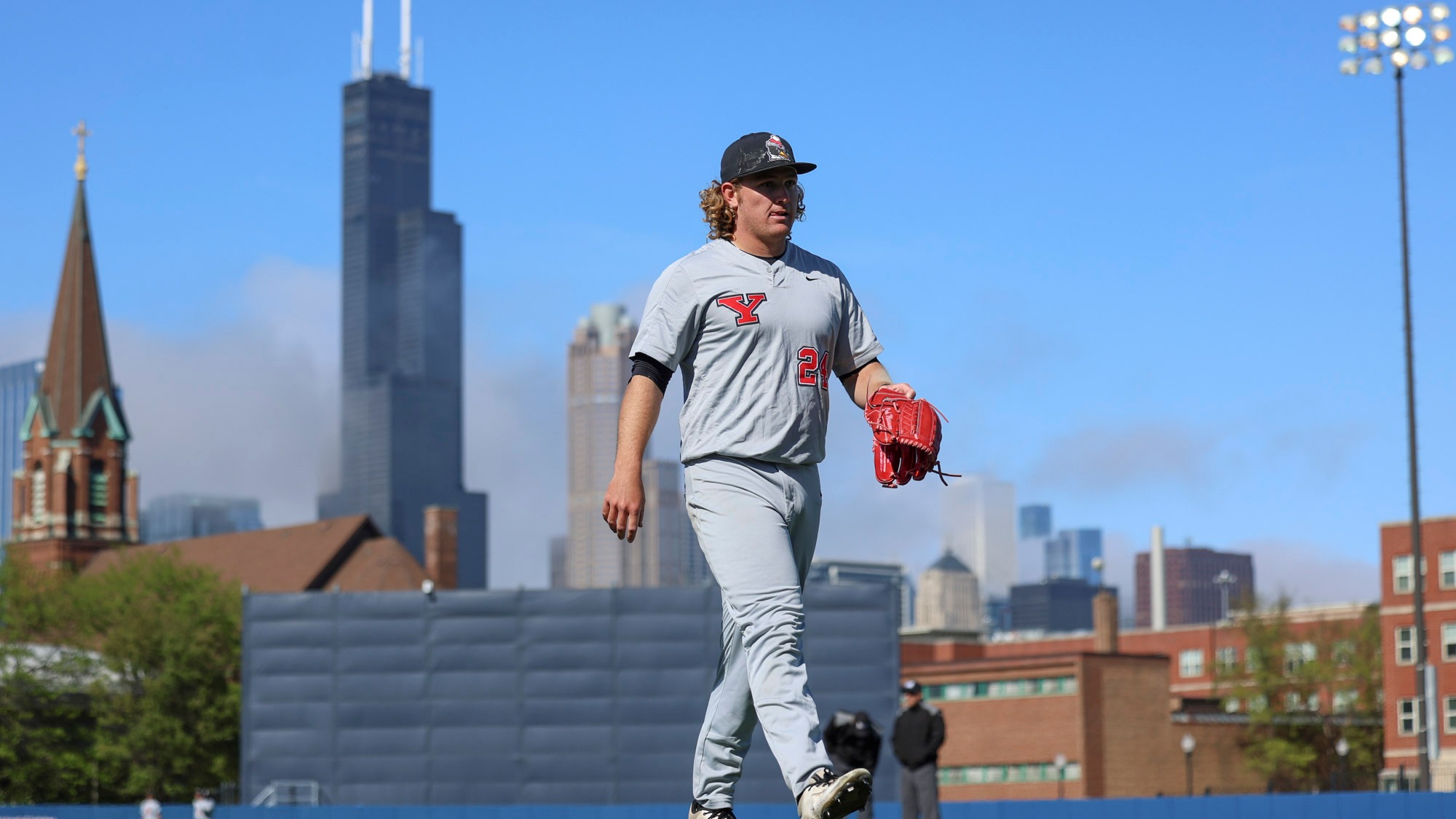 Jack Messmore walks toward the dugout at UIC with the Chicago skyline in the background.
