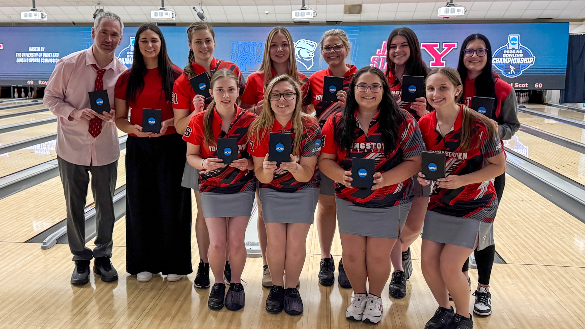 Youngstown State’s bowlers and coaches stand in front of lanes with their participant awards at the Lansing Regional.