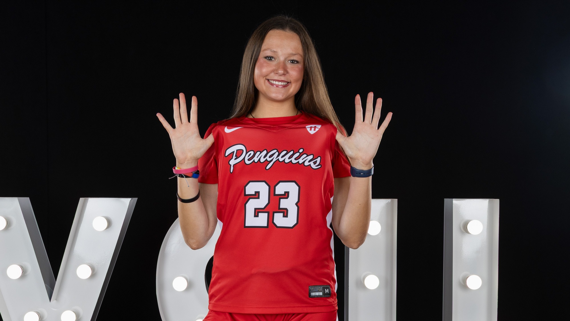 Gemma Walker pulls her jersey forward in front of a YSU sign in a photo studio setting