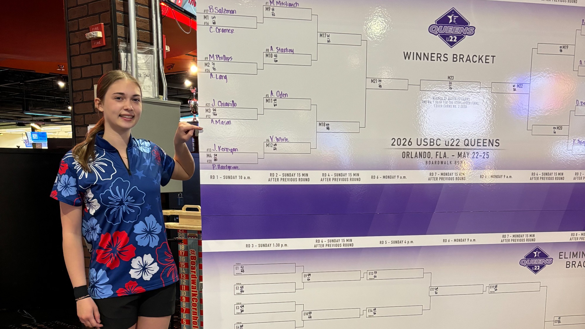 Amber Mason points to her name while standing next to the bracket of the U22 Queens event.